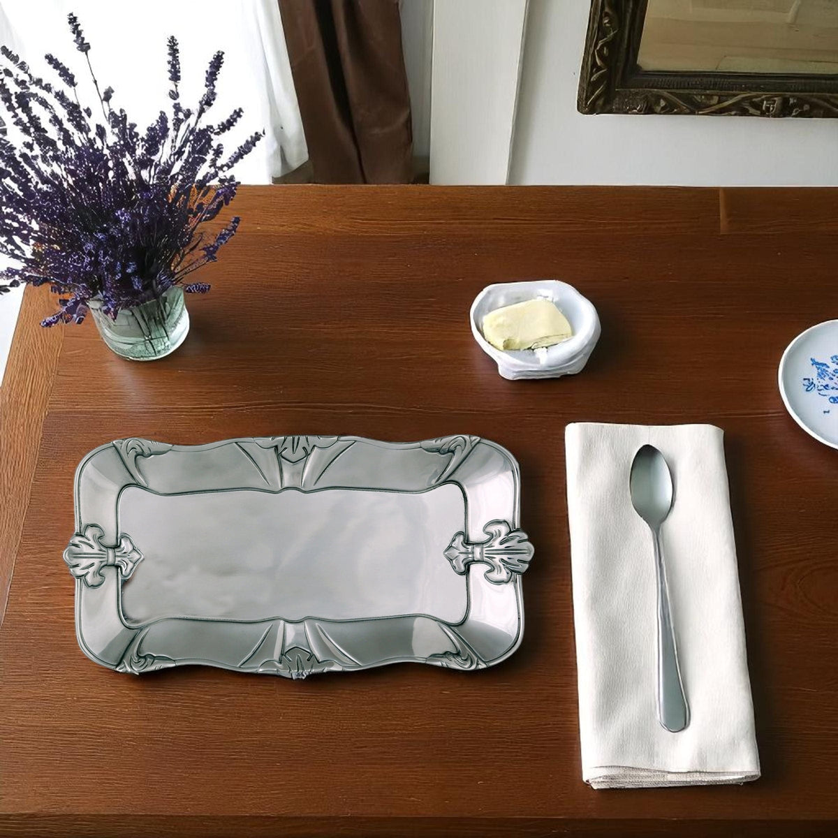 Silver tray, white napkin with spoon, bowl of butter, and lavender on a wooden table.