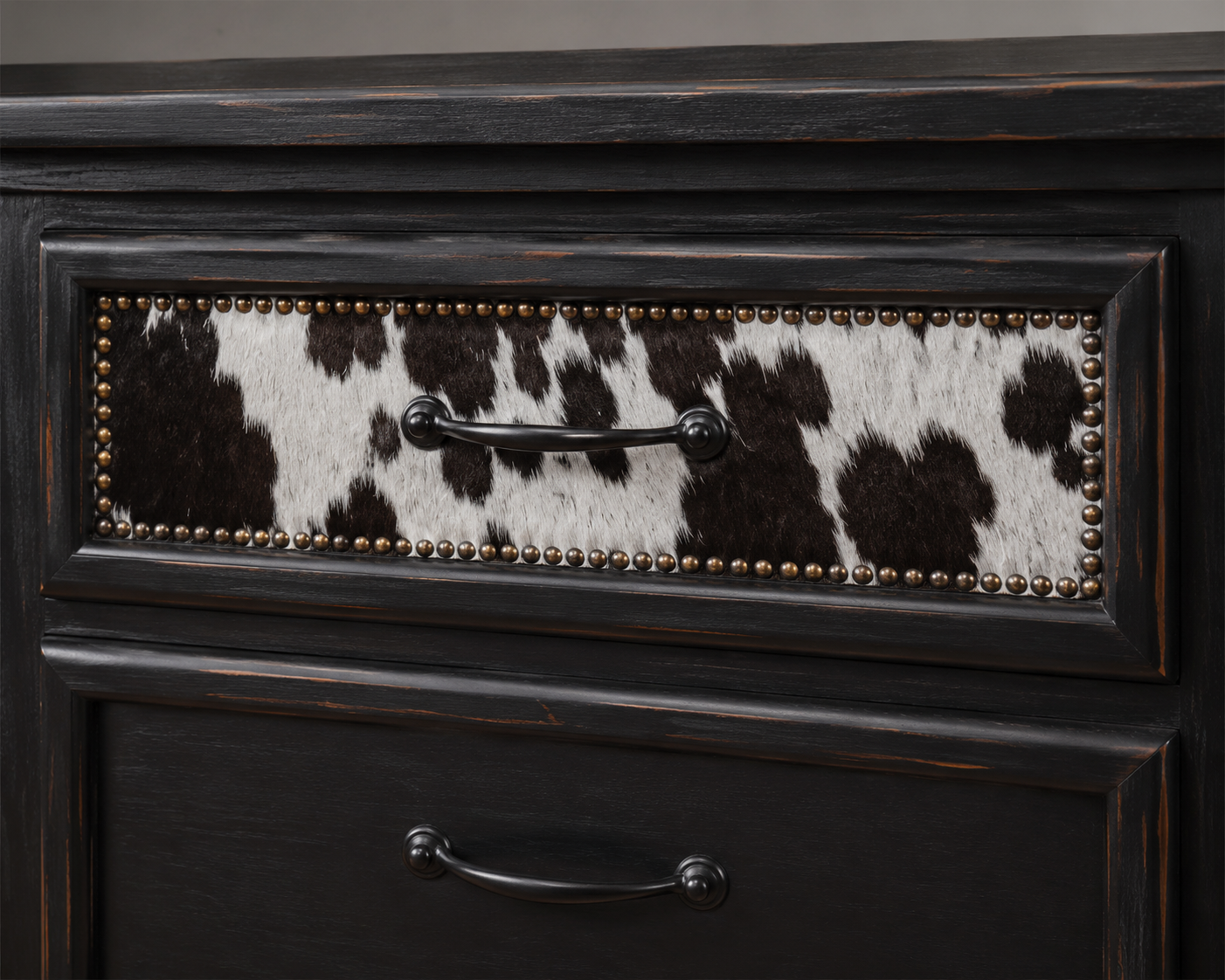 Detail of dresser drawer front with black and white cowhide upholstery and nailhead trim 