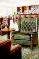 Vintage-style tufted green leather armchair in a bar setting with a wooden table and bar in the background - Your Western Decor