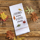 White towel with autumn-themed text and leaf designs on a wooden surface with fall leaves - Your Western Decor