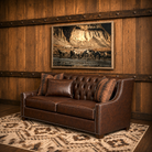 Angled view of Fort Benton tufted leather sofa with nailhead trim and patterned accent pillows