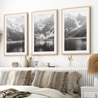 Three framed black and white mountain landscape prints above a bed with natural wood frames and white border