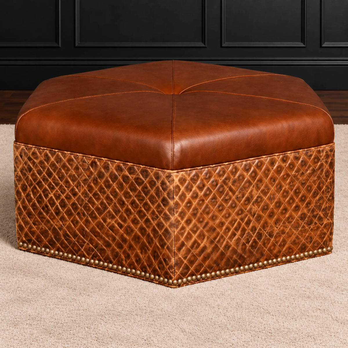 A hexagonal brown leather ottoman with a tufted top and a quilted diamond-patterned base, finished with nailhead trim, shown on a beige carpet in front of a dark paneled wall.