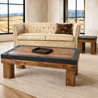 A rustic rectangular coffee table with a medium brown wood grain top and thick black metal frame accents, styled in a modern living room setting with a cream tufted sofa and a small matching side table.