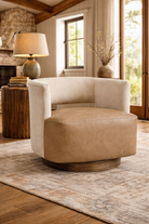 ivory cowhide and tan leather swivel chair in modern western ranch living room with wood side table and ceramic lamp on neutral rug