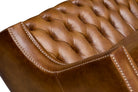 Close-up of a brown leather tufted sofa with visible stitching and nail trim 