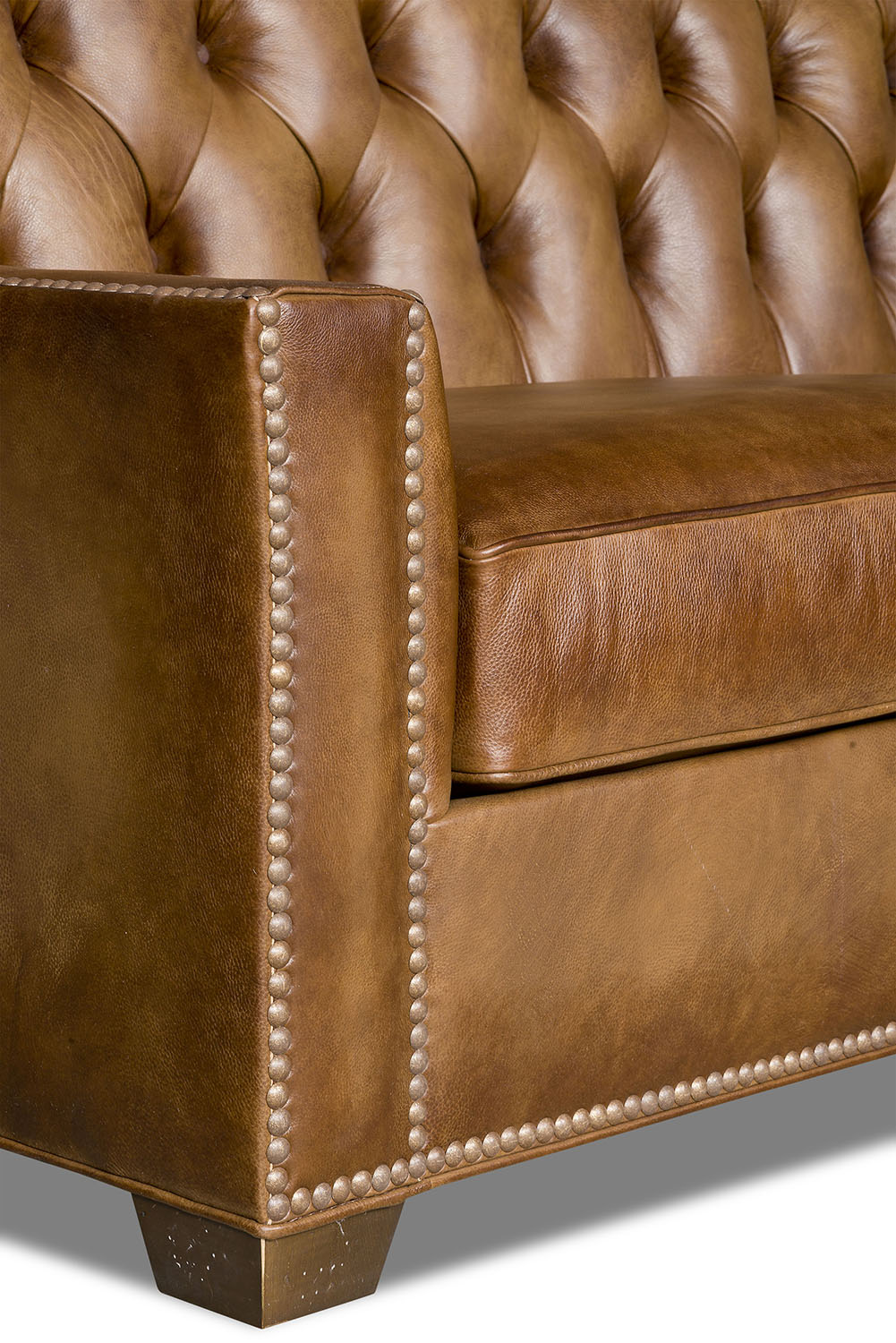 Close-up of a brown leather sofa with tufted backrest and nailhead trim.