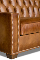 Close-up of a brown leather sofa with tufted backrest and nailhead trim.
