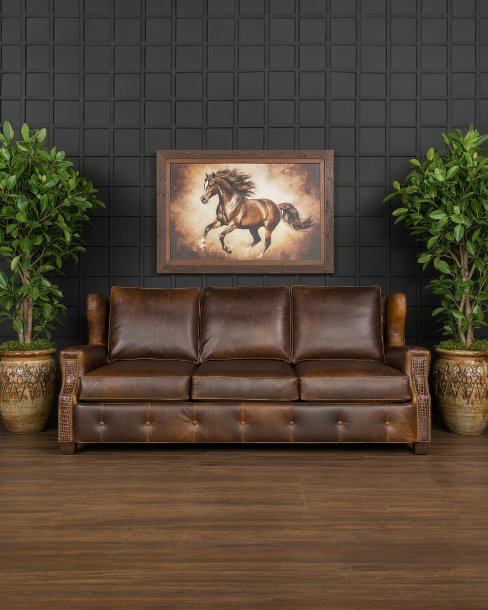 Brown leather sofa in a room with a dark wall, framed horse painting, and two potted plants 