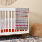 Grey lambswool folded blanket with colored striped hanging over the side of a white crib 