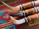 Three decorative animal horns with leather wraps on a patterned rug
