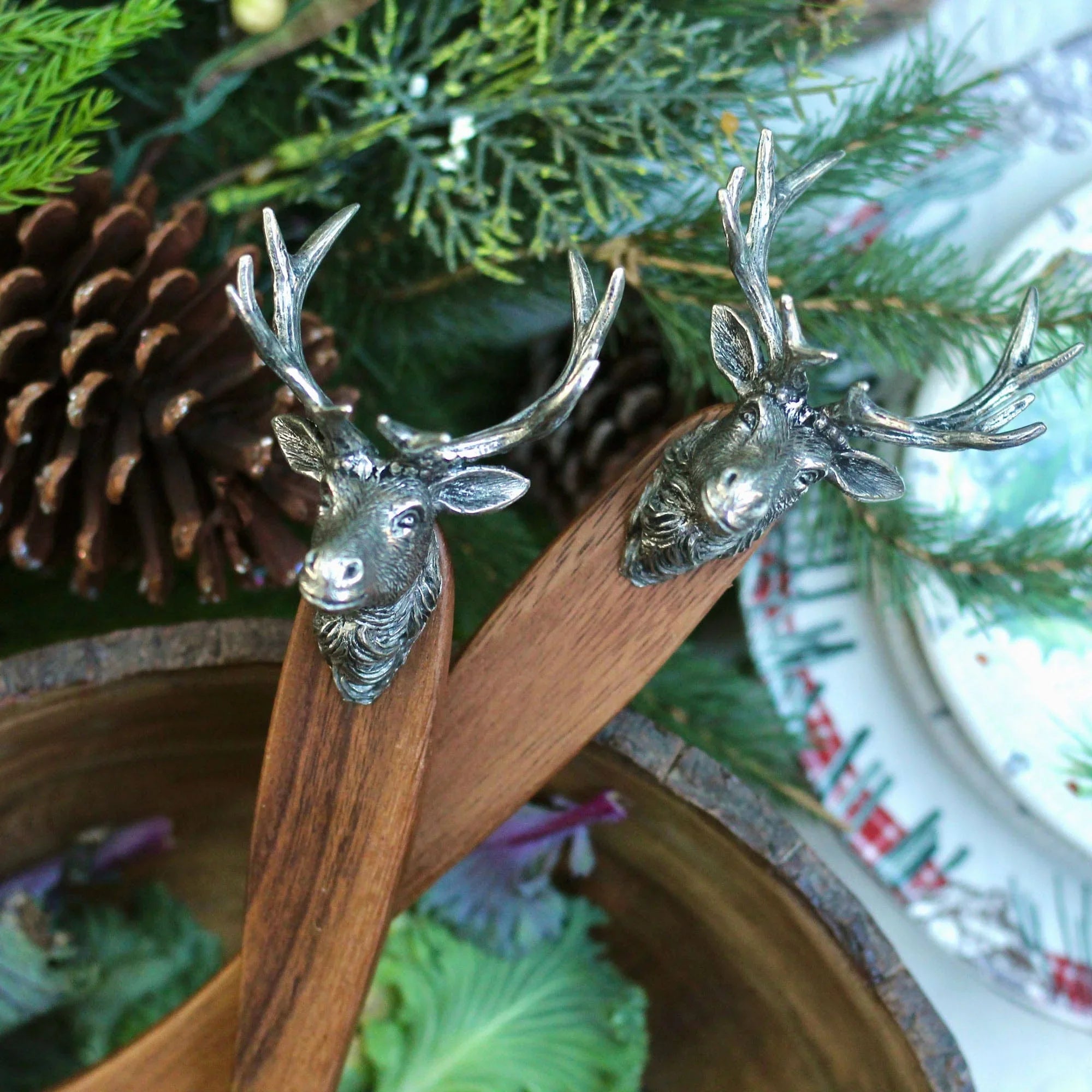 Wooden salad server set with elk head handles on a festive background with pine cones and greenery - Your Western Decor