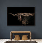 Framed artwork of a longhorn bull on a dark background in a room with a wooden bench and stools - Your Western Decor