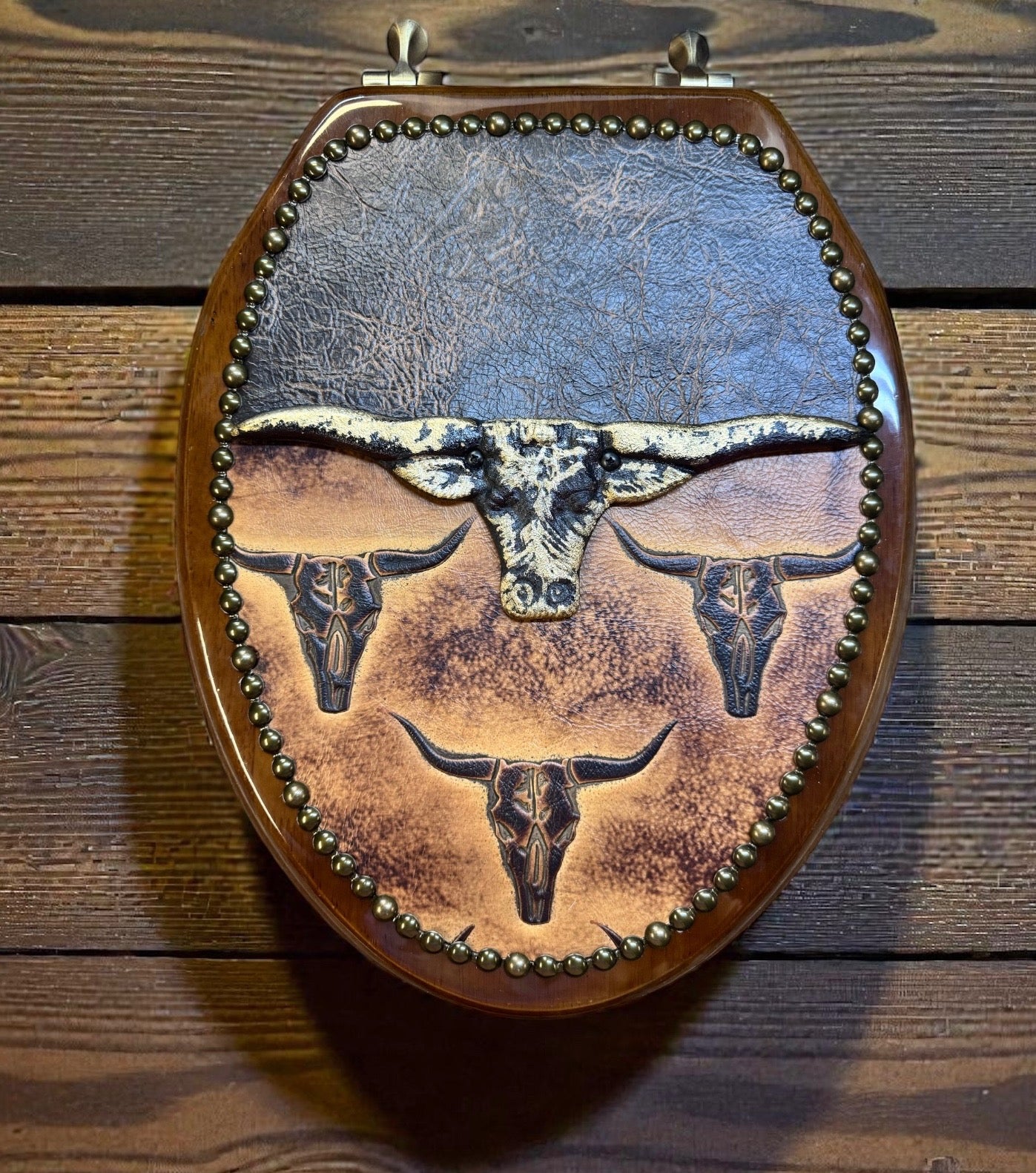 Dark wood elongated toilet seat with leather upholstery, tacking, and longhorn