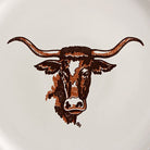 A stylized longhorn steer head illustration in dark brown and copper-brown tones on a plain white china background. Licensed artwork by Till Goodan. 