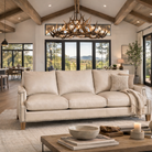 Luxury ivory leather sofa styled in open-concept ranch home with rustic wood beams, scaled antler chandelier, neutral area rug, and expansive mountain views through glass doors