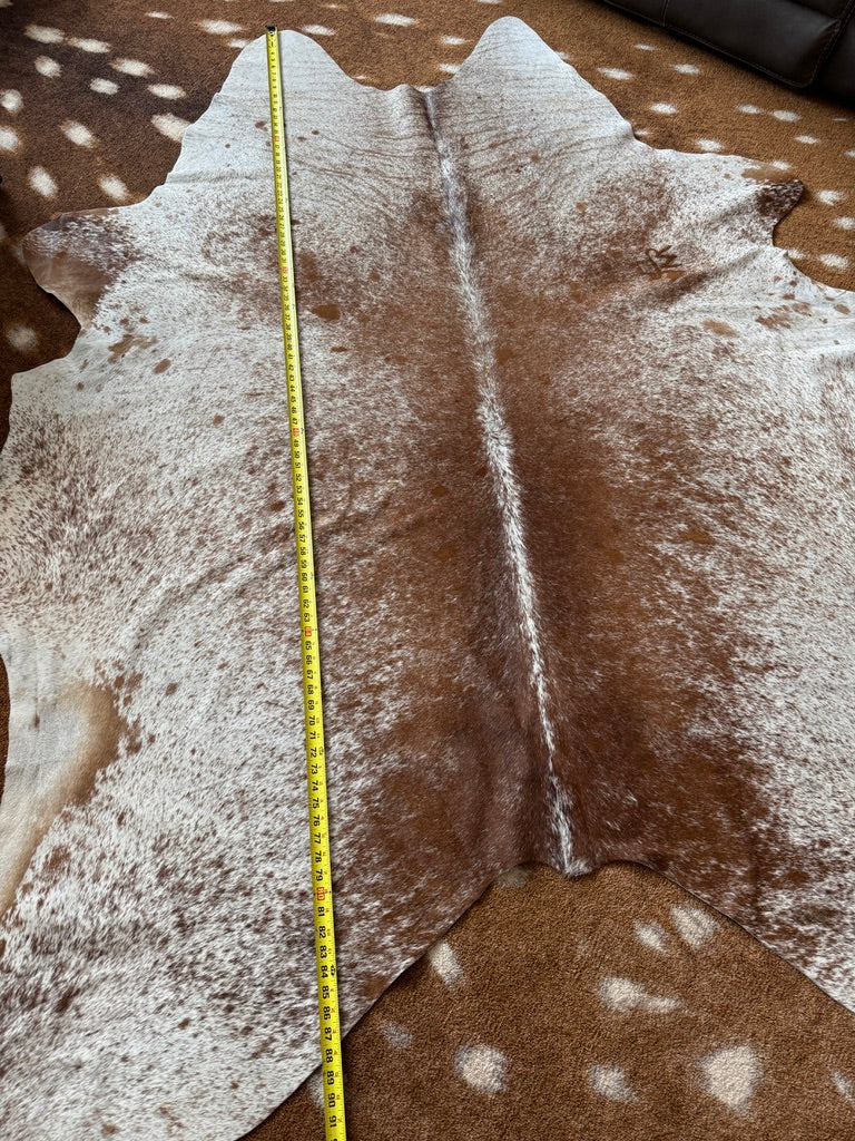 Brown cowhide rug with a measuring tape for scale on a patterned surface