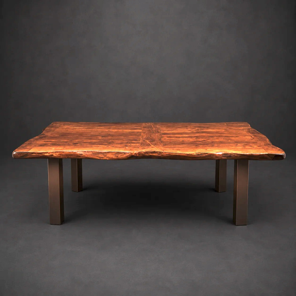 A rustic live-edge wooden table with a rich, warm brown grain pattern and four sturdy dark wrought iron legs, photographed against a dark gray studio background.