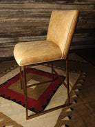 Tan leather bar stool against a wooden wall with a patterned rug below - Your Western Decor
