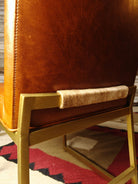 Close-up of a brown leather chair with gold frame and cowhide wrap accent on a patterned rug - Your Western Decor