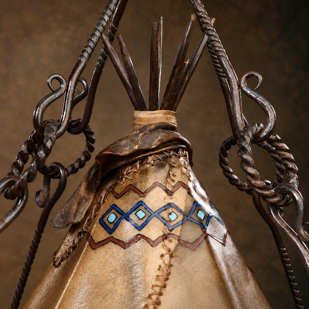 Close-up of a decorative teepee chandelier in rawhide and iron, blue and brown geometric pattern, and dark metal rope and scroll supports against a brown background.