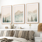 Watercolor triptych mountain scene art set with light wood frames and white border hanging above bed 