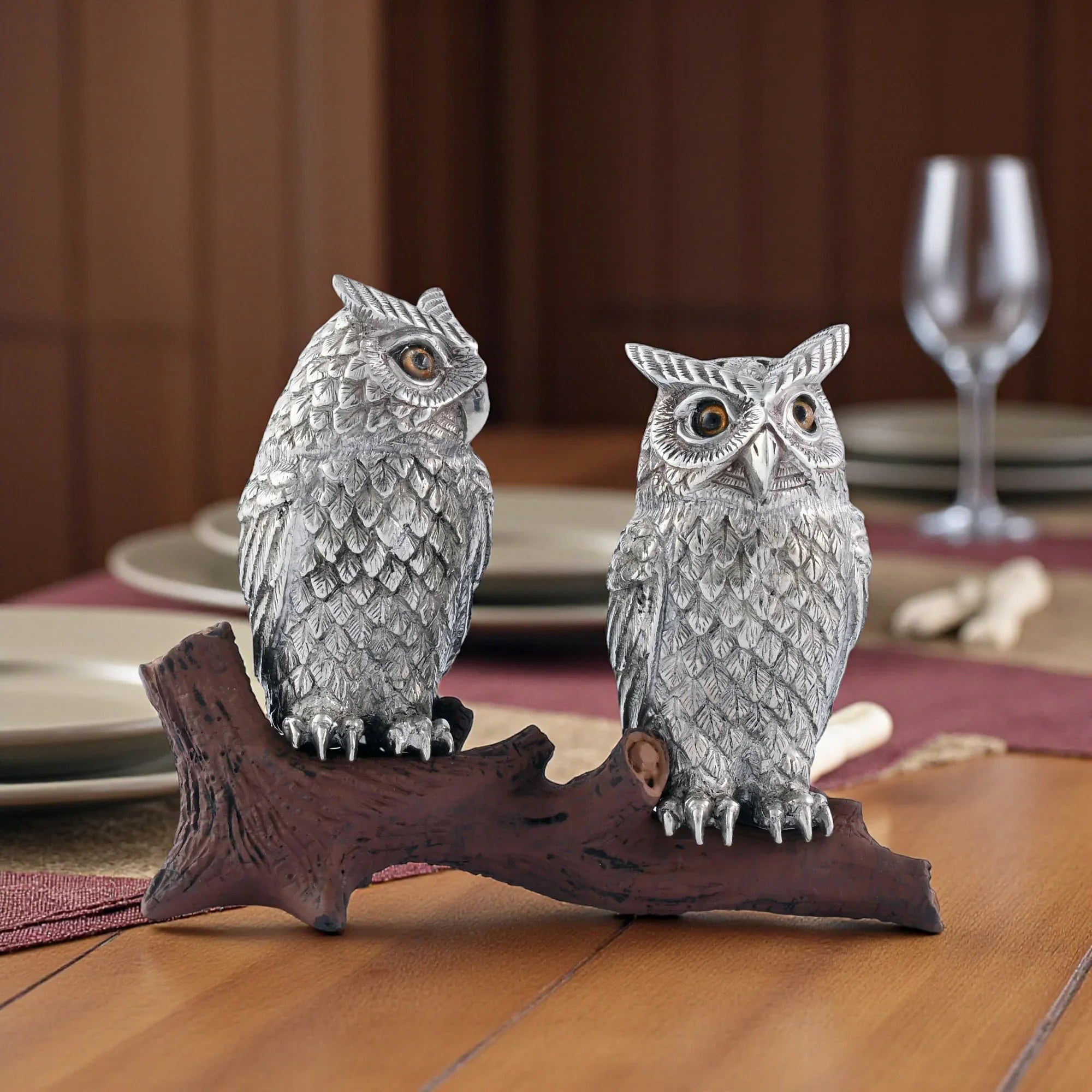 Two owl-shaped salt and pepper shakers on a wooden stand with a blurred background of a dining setting - Your Western Decor
