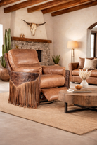 Fringed brown leather recliner with embossed leather panels and extended footrest placed in a minimalist ranch-style clubhouse lounge with natural wood beams, stone fireplace, neutral textiles, and warm ambient lighting - Your Western Decor