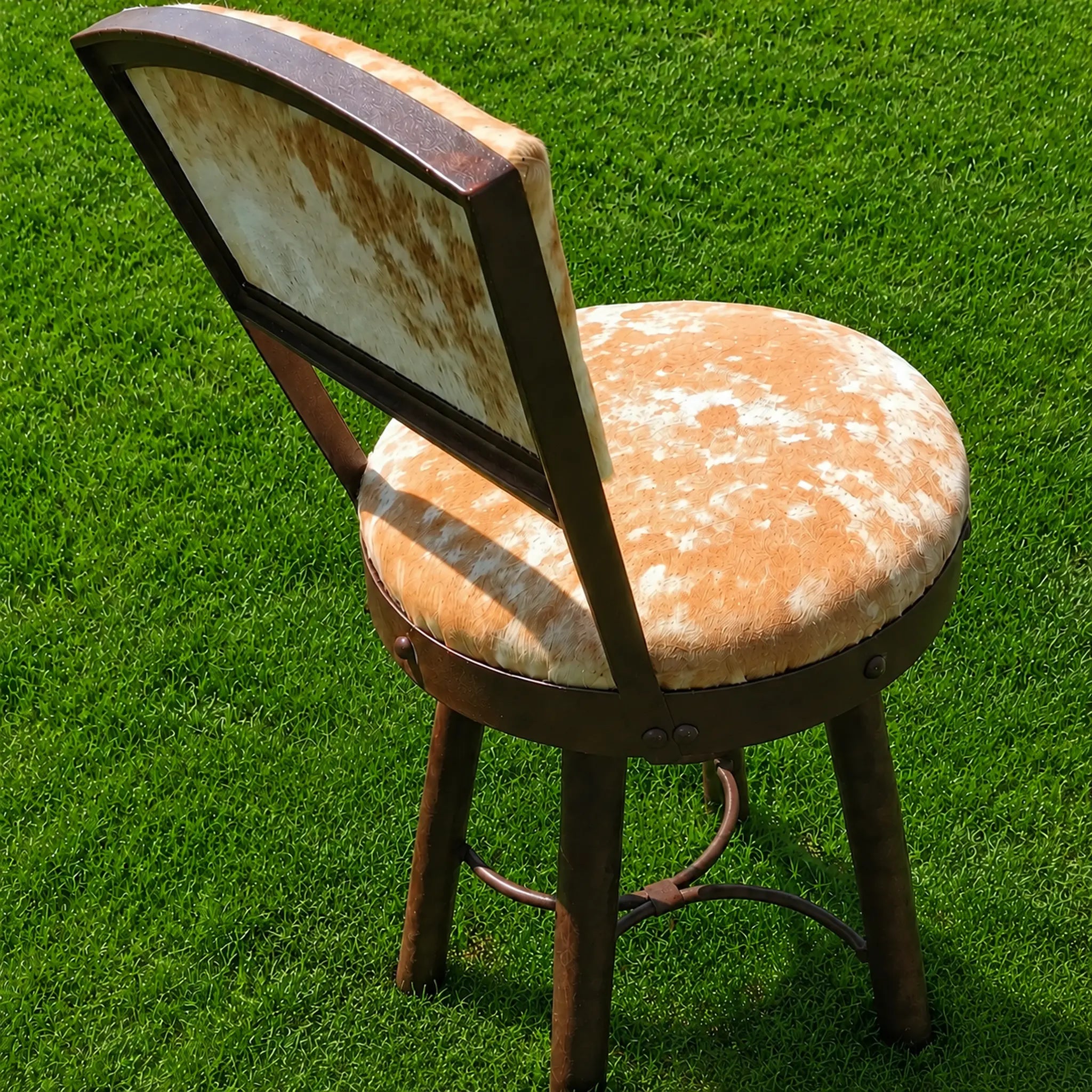A rustic bar stool with a cowhide-patterned seat and backrest, set on a vibrant green grass lawn.