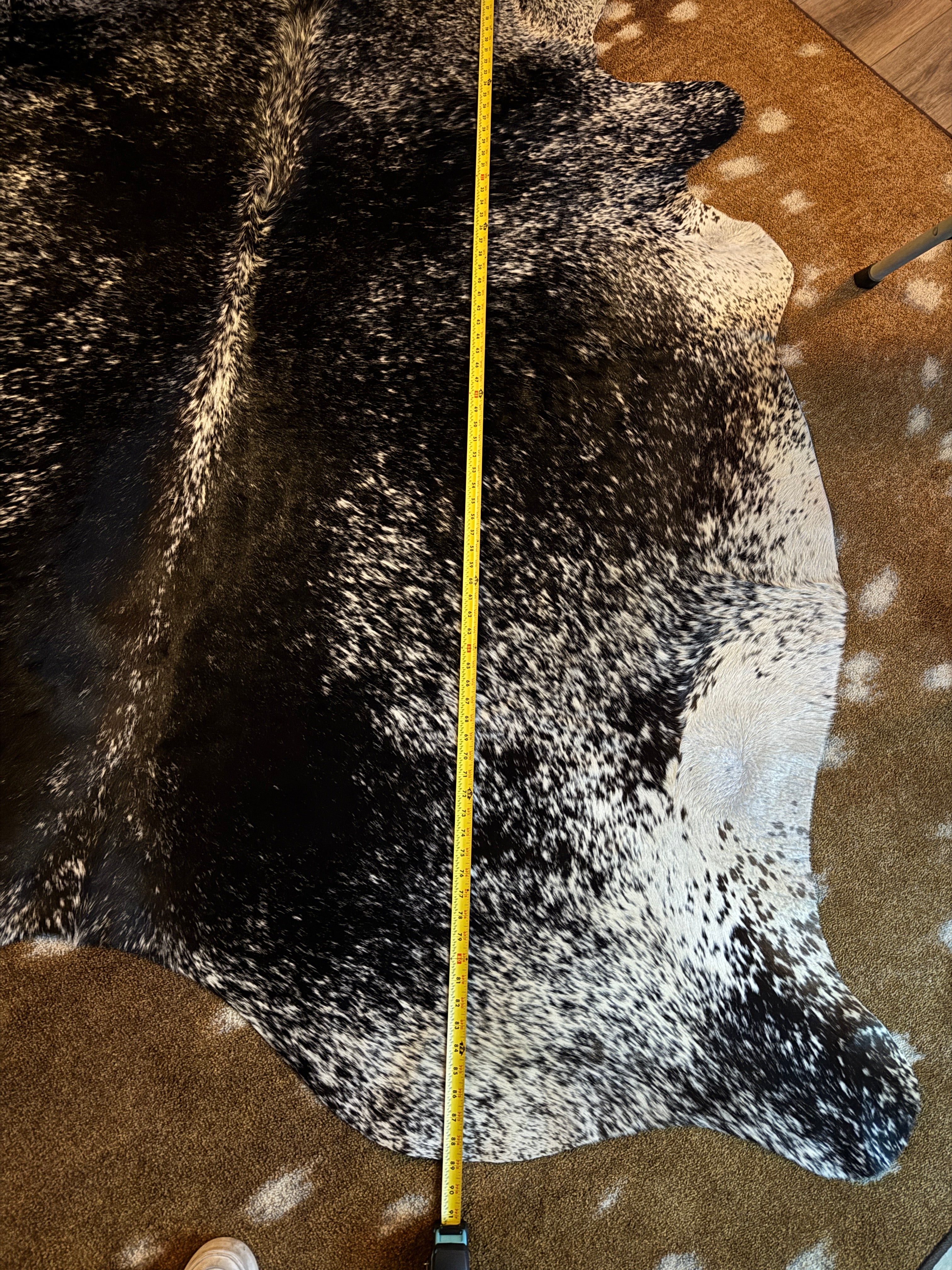 Measurement of a cowhide rug with a tape measure on a brown surface - Your Western Decor