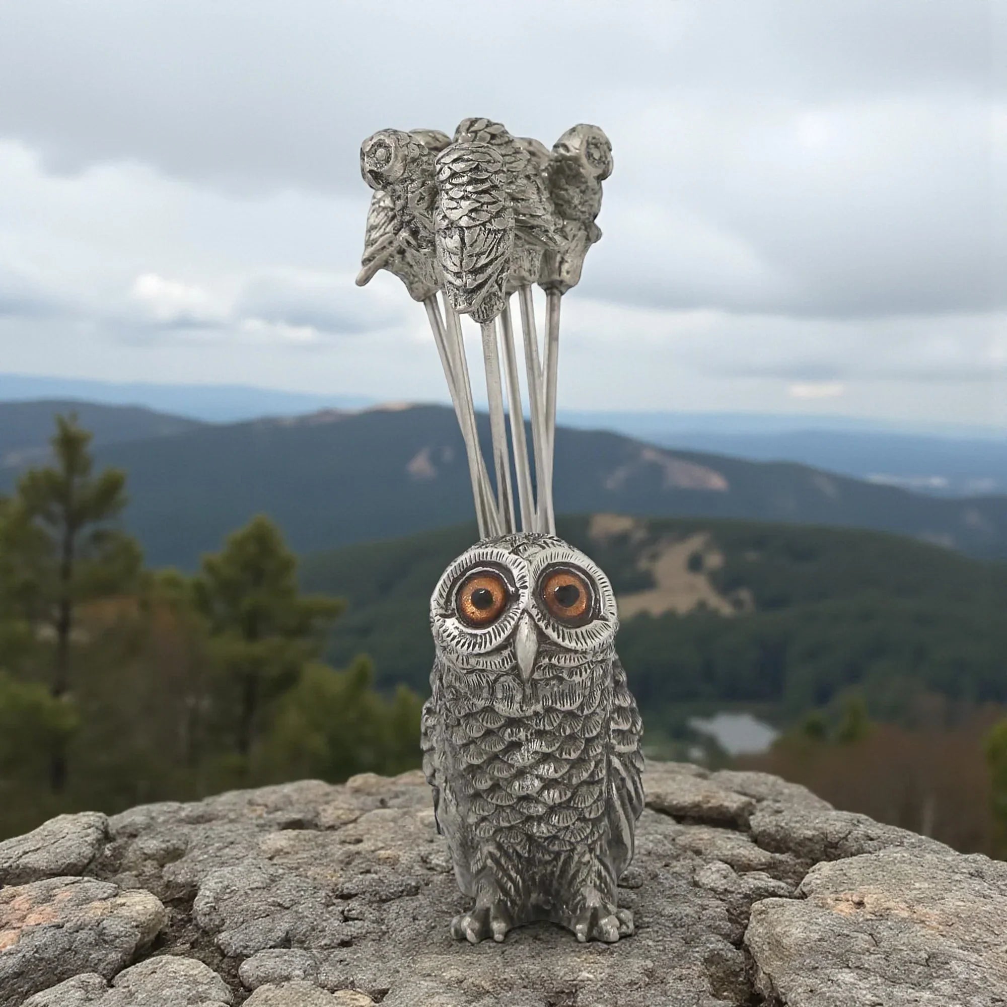 Pewter owl snack stick set on a rocky outcrop with a mountainous landscape in the background
