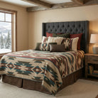 A rustic bedroom scene featuring a bed dressed in a southwestern patterned blanket with geometric designs in beige, brown, teal, and red, styled with matching patterned pillows and a dark gray tufted headboard.