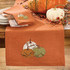 Table setting with an embroidered pumpkin design on a rust-colored table runner, surrounded by pumpkins and foliage Your Western Decor