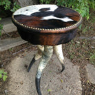 Round side table with tri color cowhide upholstery, nail trim, and steer horn legs 