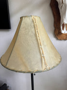 Beige rawhide lamp shade with decorative stitching on a plain wall background
