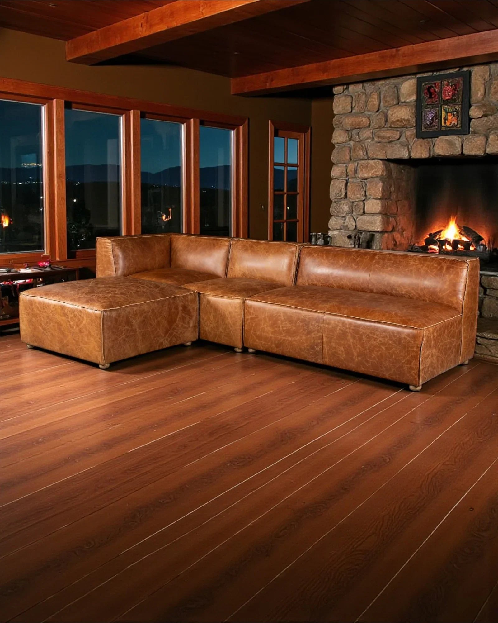 Brown leather sectional sofa in a living room with wooden floor and stone fireplace.