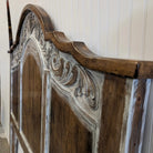 Close-up of a rustic wooden headboard with ornate carved details and a distressed white paint finish showing through the wood grain.