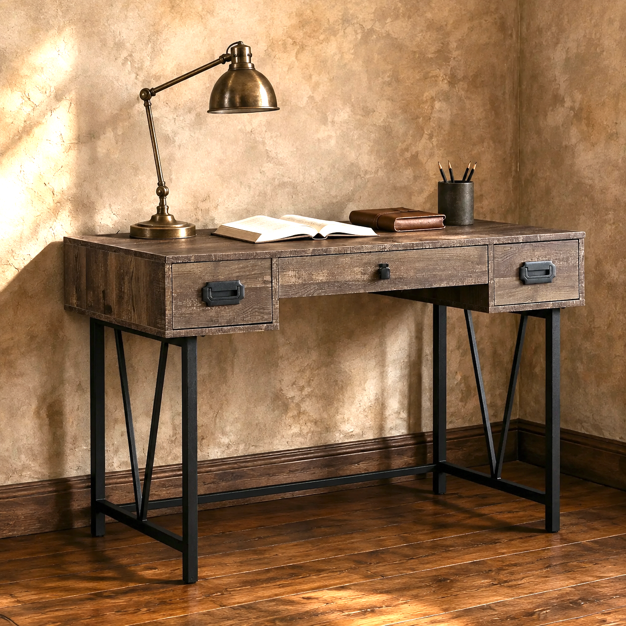 A rustic industrial-style writing desk with a weathered brown wood top, three drawers, and black metal legs, styled with a brass desk lamp, open book, and pen cup against a textured beige wall and wooden floor.