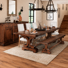 A rustic dark wood dining table with matching bench and upholstered chairs, set in a staged dining room with wood floors, a sideboard, and a chandelier.