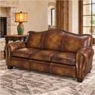 A brown burnished leather sofa with nailhead trim, shown in a rustic living room setting next to a side table with a lamp.