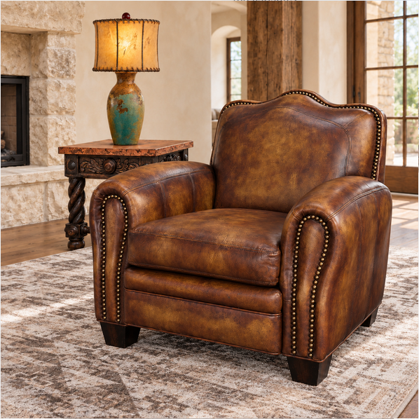 A brown leather armchair with nailhead trim, shown in a styled living room setting next to a wooden side table with a lamp.