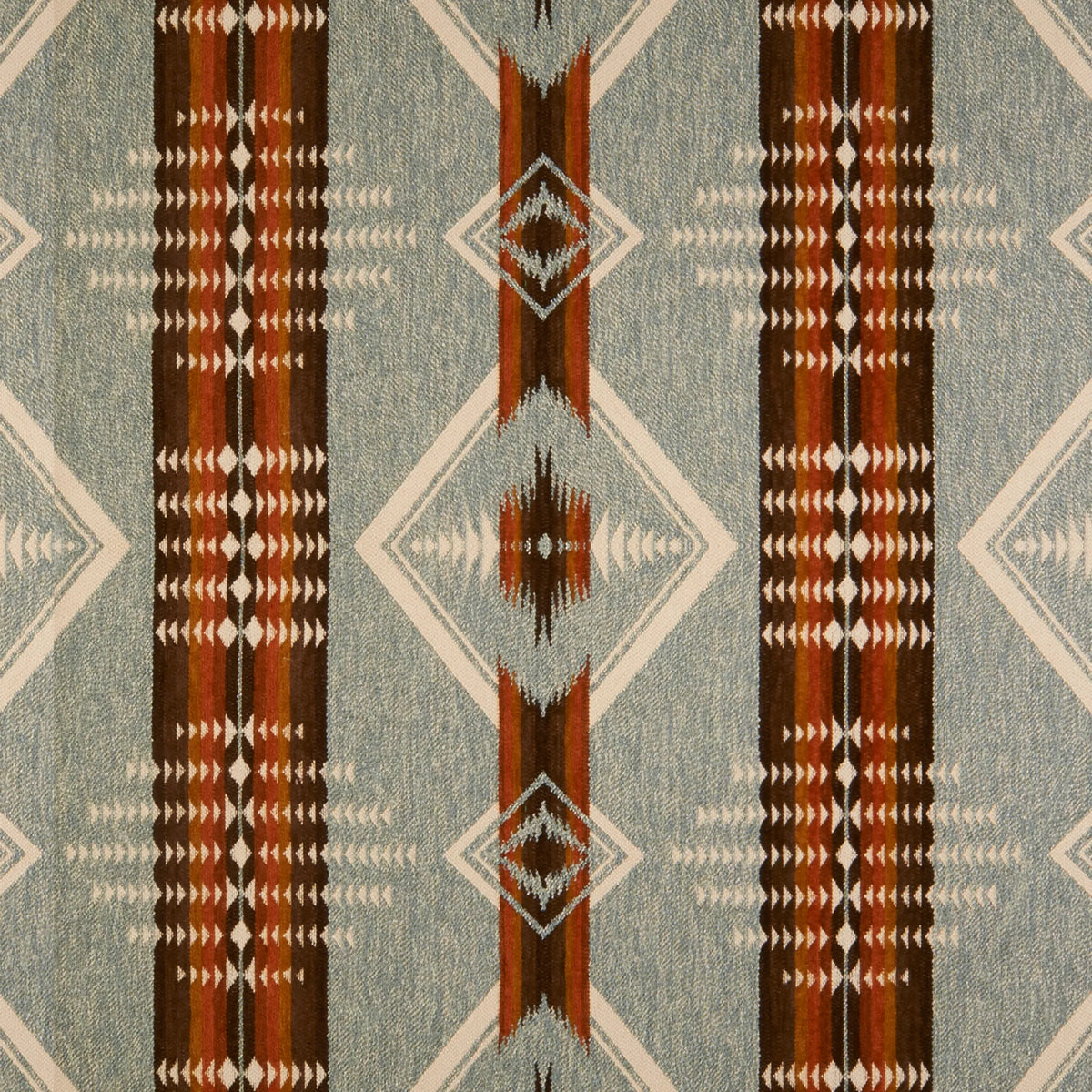 A close-up of a woven textile fabric pattern with a Southwestern geometric design. The color palette features a muted blue-gray base, vertical stripes in dark brown, rust red, and beige, and diamond motifs.