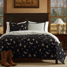 Bedroom with a bed featuring a black and white western patterned quilt, cowboy boots, and a lamp.