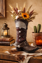 Western resin cowboy boot vase with tooled leather detailing, silver conchos, and spur accent styled on rustic wooden table with dried florals.