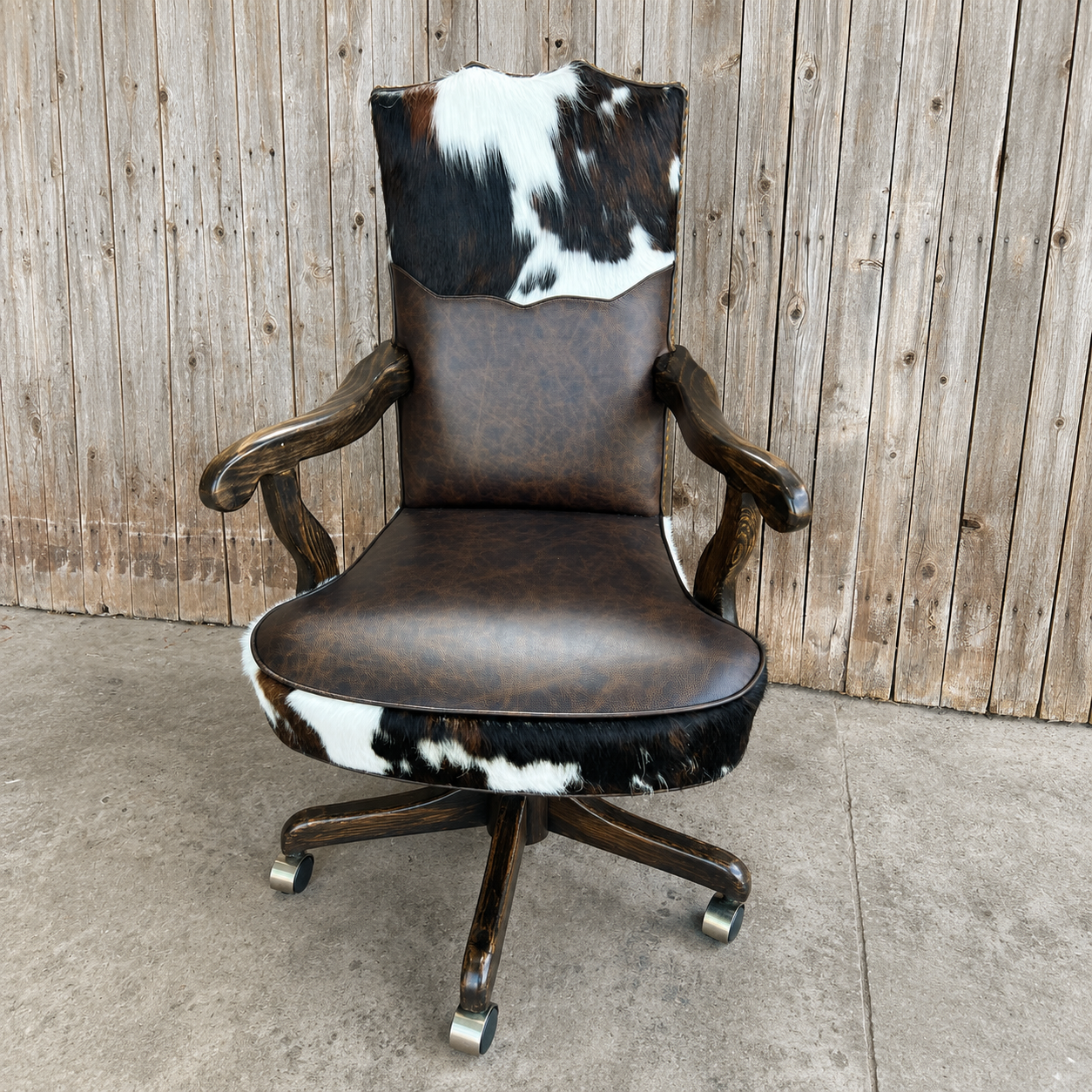 A rustic office chair with a dark brown faux-leather seat and back, featuring cowhide-patterned accents on the headrest and lower seat, mounted on a dark wood five-star swivel base with casters.