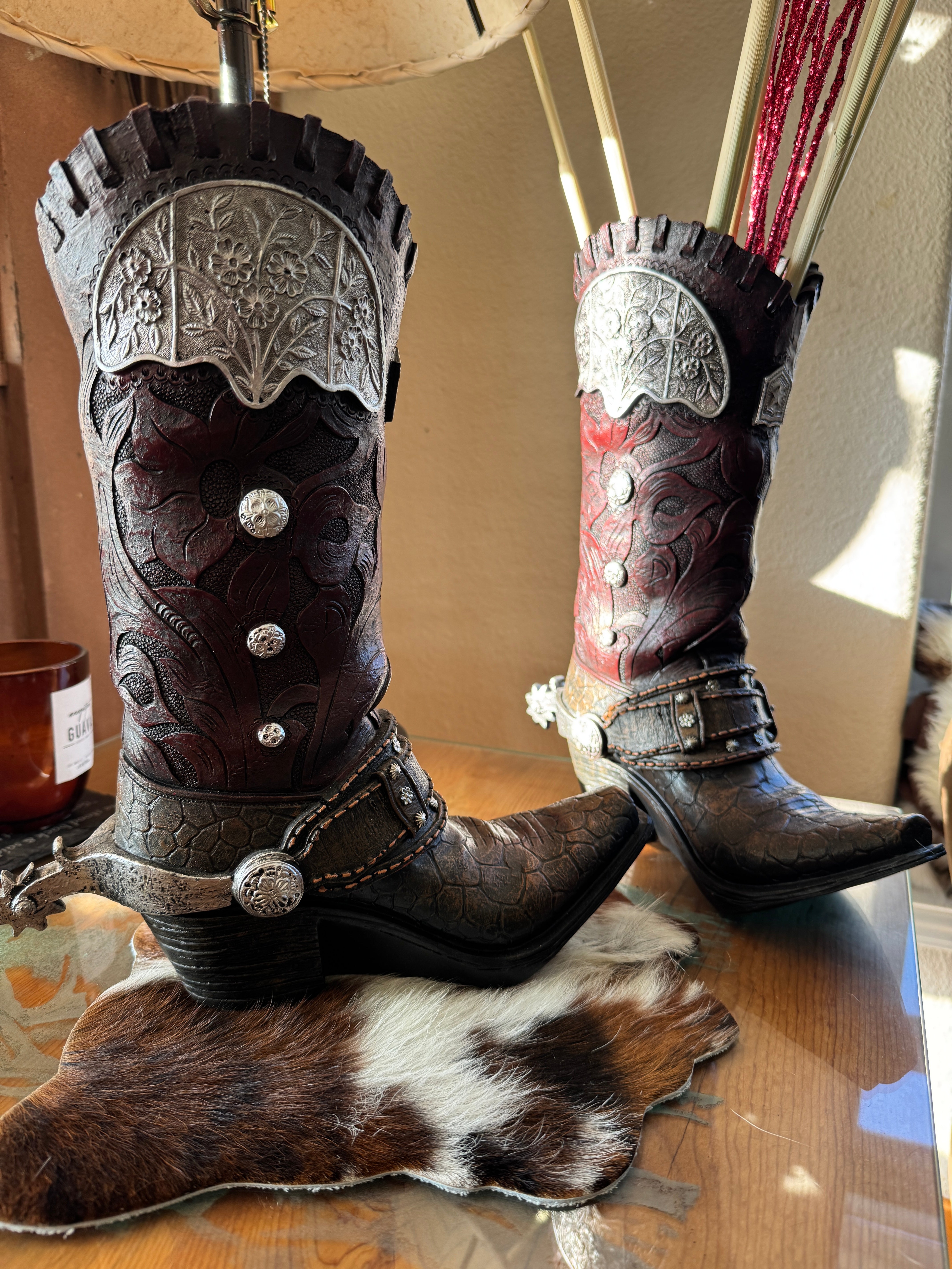 Pair of cowboy boot vases with intricate designs on a cowhide rug mat 