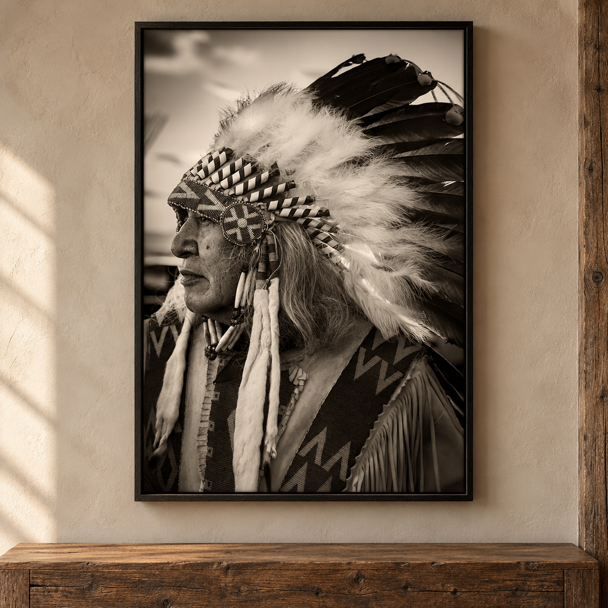 A framed black and white photographic print of a Native American man in profile with a large feathered headdress, displayed on a beige wall above a rustic wooden surface.