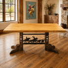 A rustic rectangular wooden dining table with a light natural wood top and a dark iron trestle base featuring cow and rider silhouettes, shown in a warm, wood-paneled room with cowboy art