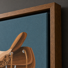 Close-up of a framed wall art print showing a stylized brown leather saddle on a textured dark teal-blue background, with a medium-brown wooden frame against a dark wall.