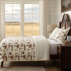 Bedroom with a bed featuring a patterned western cowboy quilt, wooden headboard, and nightstand with a lamp.